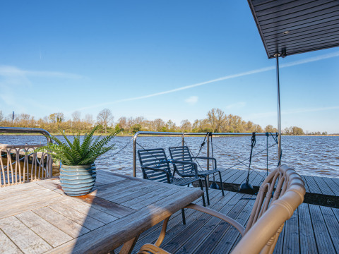 Udendørs terrasse på husbåd «Campi» ved Marina Uitgeest, med udsigt over sø og træer under blå himmel.