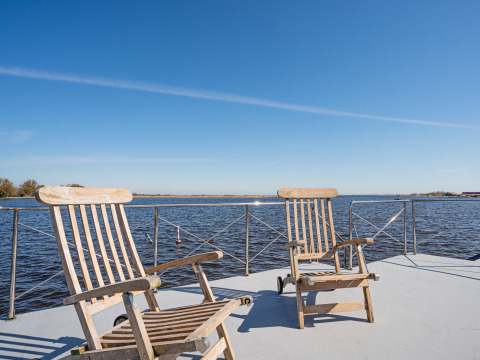 Dos sillas de madera en la cubierta de la casa flotante Campi en Marina Uitgeest, Países Bajos, con vista al agua.