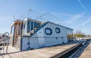 Casa flotante moderna 'Campi' atracada en Marina Uitgeest, Países Bajos, bajo un cielo soleado y claro.