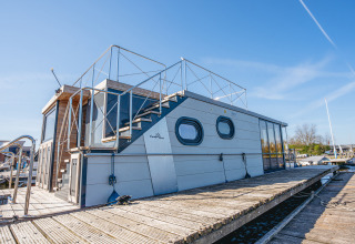 Moderne husbåd 'Campi' fortøjet ved Marina Uitgeest i Holland under en klar blå himmel.