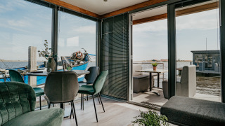 Modern interior of Houseboat Havenlodge with glass walls, water views, and a sunny terrace outside.
