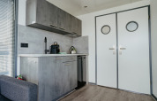 Modern kitchenette with grey cabinets and double doors in Houseboat «Havenlodge» at Marina Uitgeest in the Netherlands.