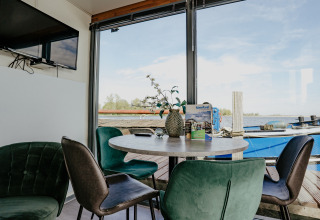 Sala con mesa redonda, sillas verdes y vista al lago en la Houseboat Havenlodge en Marina Uitgeest, Países Bajos.