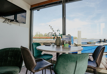 Salon avec table ronde, chaises vertes et vue sur le lac à bord du Houseboat Havenlodge à Marina Uitgeest.