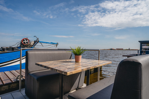 Udendørs siddeområde med bord og planter på husbåden Havenlodge i Marina Uitgeest, Holland, udsigt til vand.