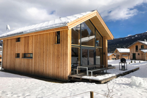 Houten chalet Kreischberg Chalets 28 met grote ramen en besneeuwd dak, gelegen in een winterse bergomgeving.
