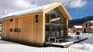 Houten chalet Kreischberg Chalets 28 met grote ramen en besneeuwd dak, gelegen in een winterse bergomgeving.