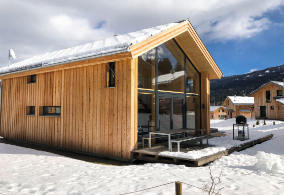 Houten chalet Kreischberg Chalets 28 met grote ramen en besneeuwd dak, gelegen in een winterse bergomgeving.