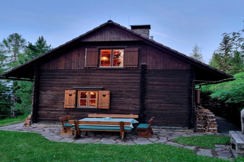 Foto einer gemütlichen Holzhütte namens Schneiderhütte mit Gartensitzgruppe im Wald in Österreich.
