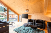 Salon lumineux du Kreischberg Chalets 28 en Autriche avec intérieur bois, fauteuils en cuir noir et grandes fenêtres.