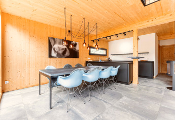 Salle à manger moderne de chalet avec chaises bleues, table noire, murs en bois et lampes stylées en Autriche.
