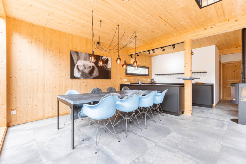 Moderne chalet-eetkamer met lichtblauwe stoelen, zwarte tafel, houten wanden en stijlvolle lampen in Oostenrijk.