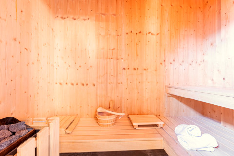 Interno sauna in legno chiaro con secchio, pietre, panche e asciugamani a Kreischberg Chalets 28, Austria.