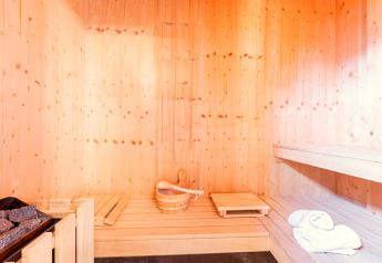 Intérieur de sauna en bois clair avec seau, pierres, bancs et serviettes, Kreischberg Chalets 28 en Autriche.