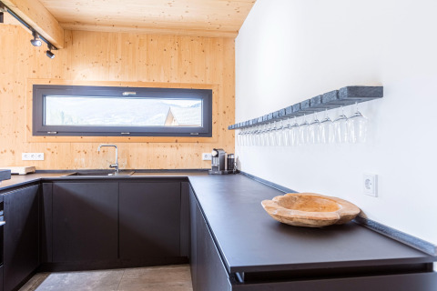 Moderne keuken in Kreischberg Chalets 28, Oostenrijk, met zwarte kasten en glazenrek aan de muur.