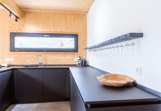 Moderne keuken in Kreischberg Chalets 28, Oostenrijk, met zwarte kasten en glazenrek aan de muur.