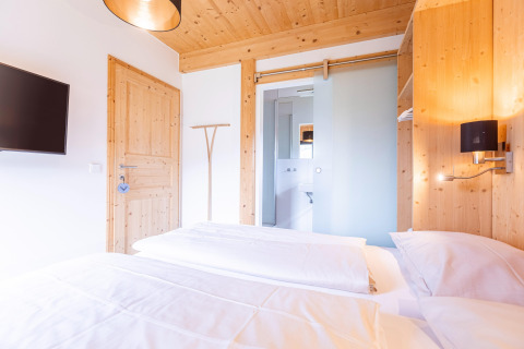 Slaapkamer met houten details, tweepersoonsbed, tv en ensuite badkamer in Kreischberg Chalets 28, Oostenrijk.