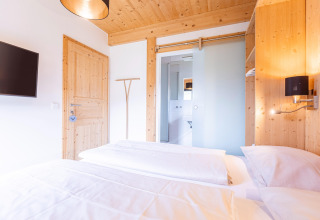 Slaapkamer met houten details, tweepersoonsbed, tv en ensuite badkamer in Kreischberg Chalets 28, Oostenrijk.