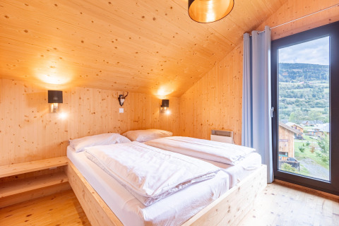 Lichte houten slaapkamer in Kreischberg Chalets 28, Oostenrijk, met uitzicht op de bergen door groot raam.
