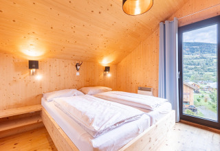 Lichte houten slaapkamer in Kreischberg Chalets 28, Oostenrijk, met uitzicht op de bergen door groot raam.