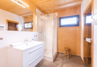 Moderne houten badkamer bij Kreischberg Chalets 28 in Oostenrijk met douche, wastafel en krukje.