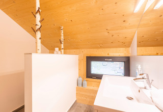 Moderne badkamer met licht houten plafond, raam en berkenstammen in Kreischberg Chalets 28, Oostenrijk.
