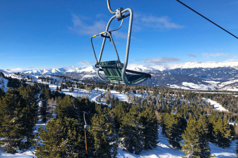Stoeltjeslift boven besneeuwde bossen en bergen, foto genomen bij Kreischberg Chalets 28 in Oostenrijk bij helder weer.