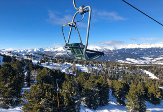 Stoeltjeslift boven besneeuwde bossen en bergen, foto genomen bij Kreischberg Chalets 28 in Oostenrijk bij helder weer.