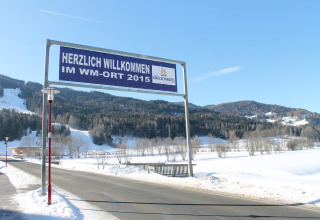 Willkommensschild am Straßenrand in Kreischberg, WM-Ort 2015, mit verschneiten Bergen im Hintergrund.