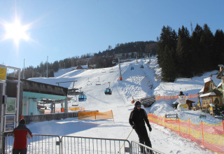 Skifahrer an einem verschneiten Skigebiet mit Seilbahn und Glamping-Unterkunft an einem sonnigen Tag.