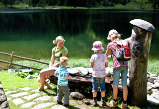 Een familie ontspant bij een berghut aan een meer, terwijl de kinderen buiten in de zon spelen.