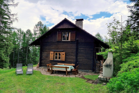 Chalet Schneiderhütte nel bosco con arredi da giardino in legno, sdraio e camino da esterno.