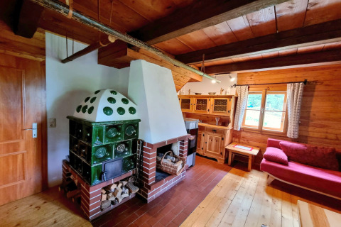 Soggiorno accogliente nello chalet Schneiderhütte in Austria con stufa in maiolica verde e arredi in legno.