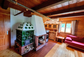 Soggiorno accogliente nello chalet Schneiderhütte in Austria con stufa in maiolica verde e arredi in legno.