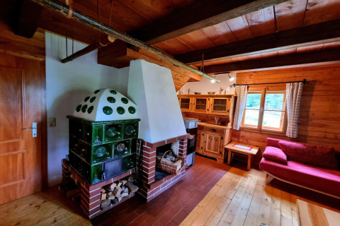 Gemütliches Wohnzimmer in der Schneiderhütte in Österreich mit grünem Kachelofen und Holzmöbeln.