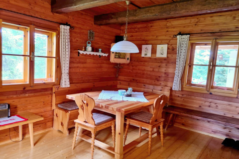Accogliente angolo pranzo in legno con panche, sedie e finestre nello chalet Schneiderhütte, Austria.