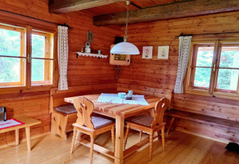 Hyggelig træhytte spisestue med hjørnebænk, træstole, vinduer og gardiner i Schneiderhütte, Østrig.