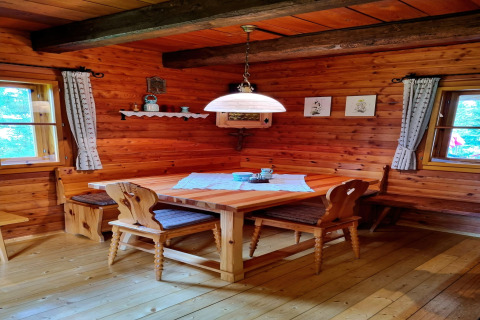 Gemütliche Stube mit Holzwänden, Eckbank und handgefertigten Stühlen in der Schneiderhütte, Österreich.