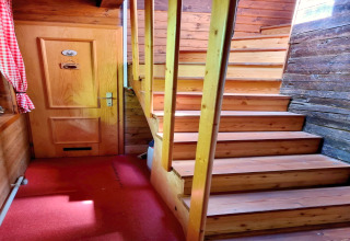 Interno dello chalet Schneiderhütte in Austria con scala in legno, porta e tappeto rosso.