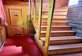 Indendørs billede af Schneiderhütte chalet i Østrig, viser en trætrappe og en dør med rødt tæppe.
