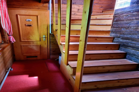 Innenaufnahme aus dem Chalet Schneiderhütte in Österreich mit Holztreppe, Tür und rotem Teppichboden.