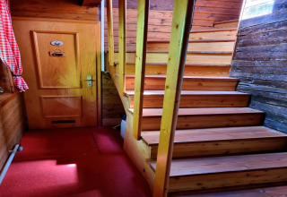 Innenaufnahme aus dem Chalet Schneiderhütte in Österreich mit Holztreppe, Tür und rotem Teppichboden.