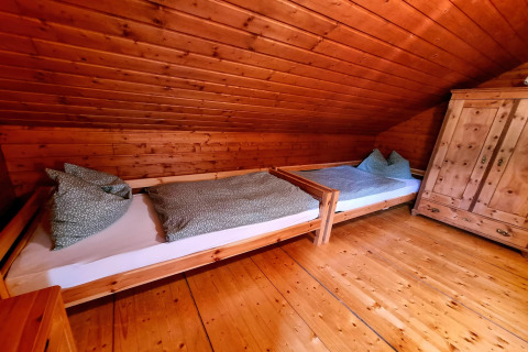 Holzvertäfeltes Zimmer im Chalet Schneiderhütte, Österreich, mit zwei Einzelbetten und Schrank.