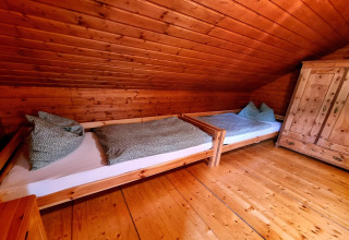Holzvertäfeltes Zimmer im Chalet Schneiderhütte, Österreich, mit zwei Einzelbetten und Schrank.