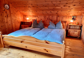 Soveværelse i Schneiderhütte-chalet i Østrig med trævægge, dobbeltseng, natborde og lamper.