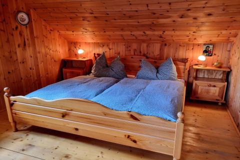 Schlafzimmer im Schneiderhütte-Chalet in Österreich mit Holzwänden, Doppelbett und Nachttischen.