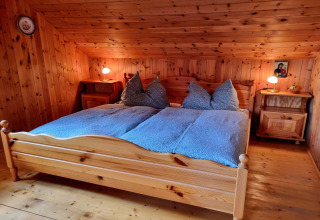 Schlafzimmer im Schneiderhütte-Chalet in Österreich mit Holzwänden, Doppelbett und Nachttischen.