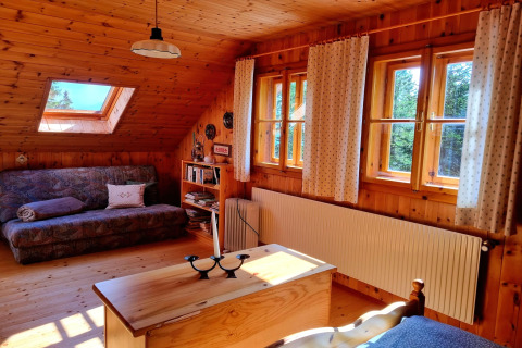 Gemütliches Chaletzimmer mit Holzverkleidung, Sofa und großen Fenstern in der Schneiderhütte, Österreich.