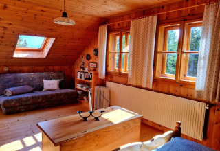 Gemütliches Chaletzimmer mit Holzverkleidung, Sofa und großen Fenstern in der Schneiderhütte, Österreich.