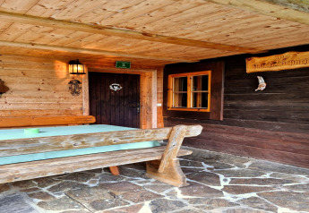 Udendørs område ved Schneiderhütte chalet i Østrig, træbænk, bord og stenbelagt terrasse.